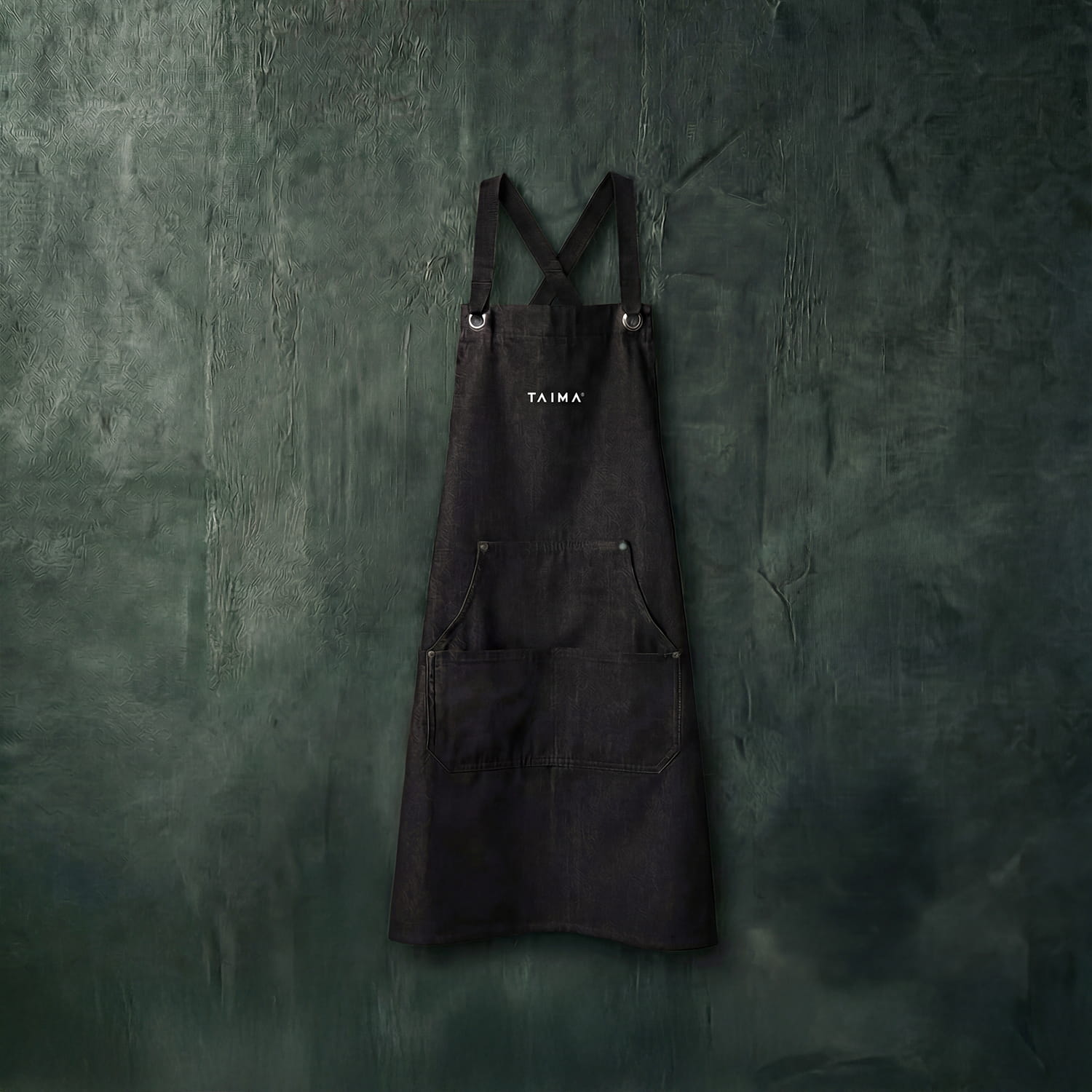 Black apron with 'Taima' branding on a textured green wall