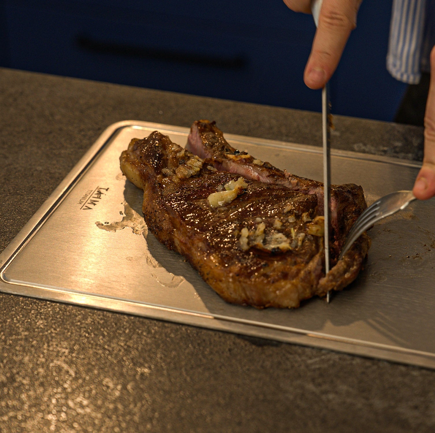 Steak being cut on a Titanium cutting board with a knife and fork.