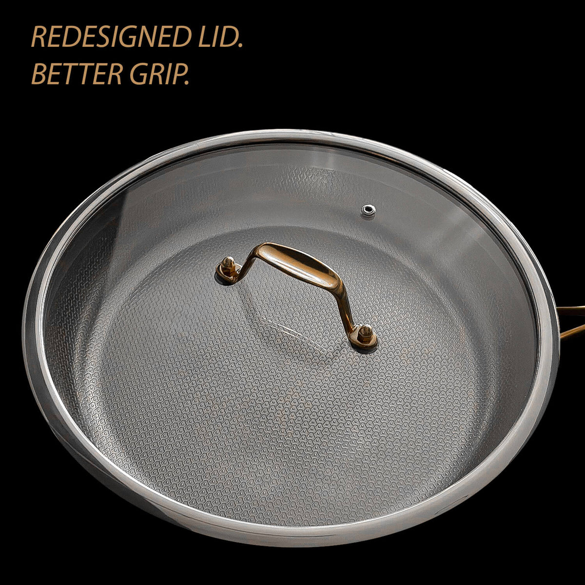 A close up of a round cookware lid with a textured silver gray surface and a metallic gold handle, shown on a black background with the text 'REDESIGNED LID. BETTER GRIP.