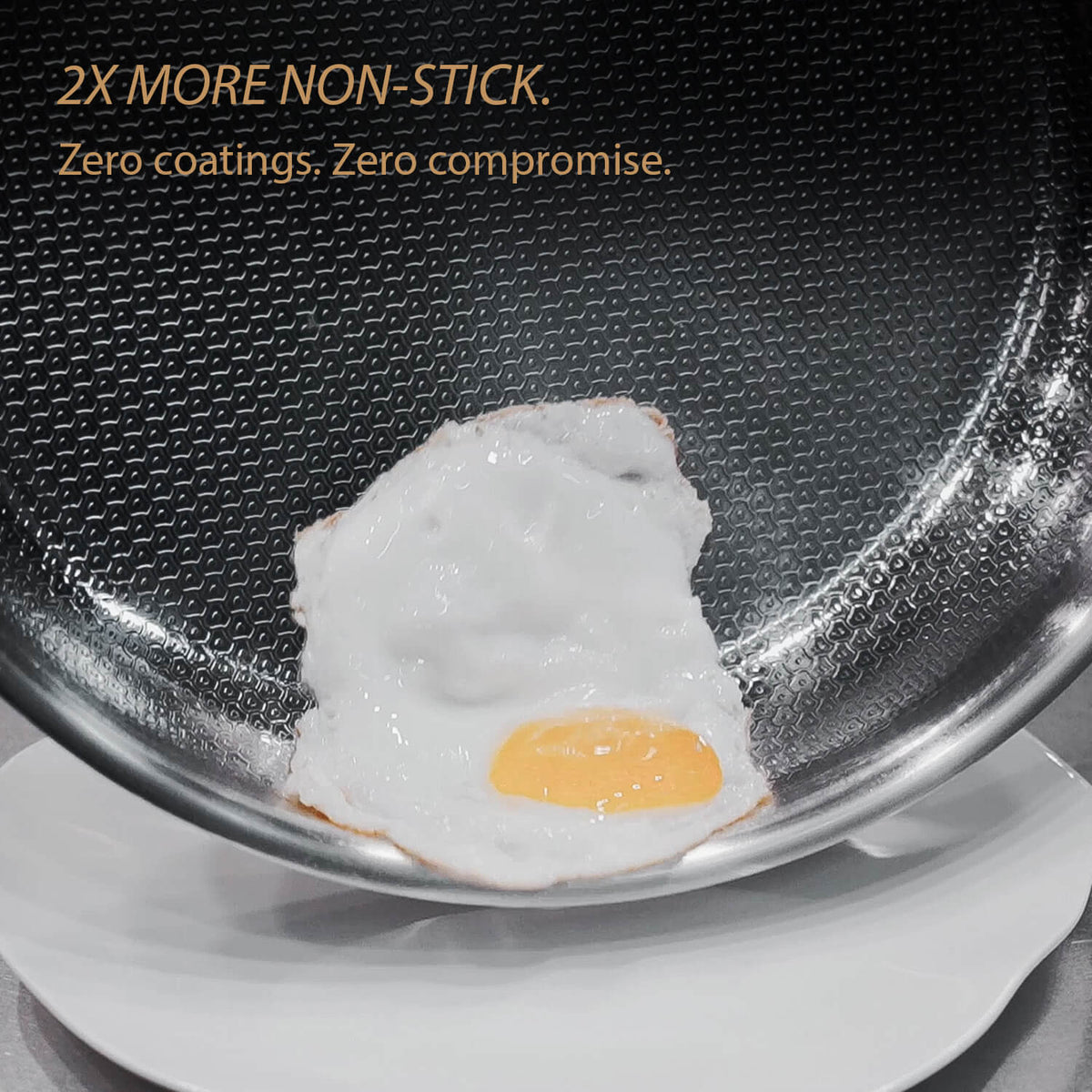 Close-up of a frying pan with a sunny-side-up egg cooking inside, with text at the top reading '2X MORE NON-STICK. Zero coatings.