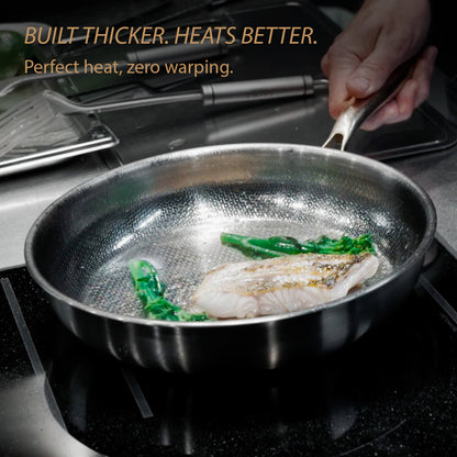 A stainless steel frying pan with a textured interior sits on a stovetop, cooking fish and green vegetables. A hand holds the handle, and promotional text at the top reads 'BUILT THICKER.