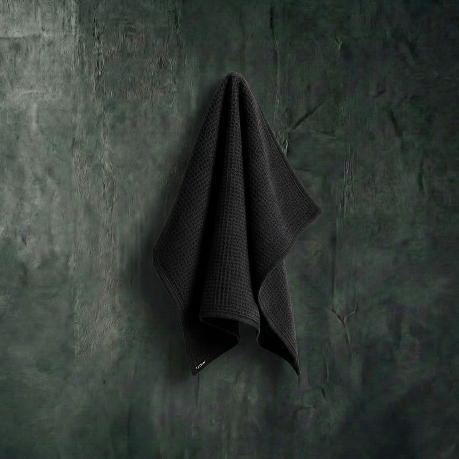 Dark gray towel hanging on a textured green wall